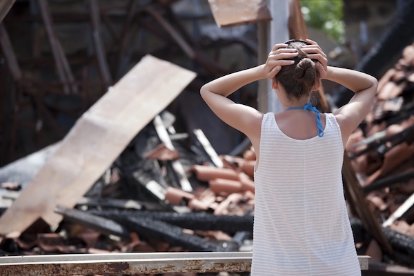 Woman standing in front of burned out house and holding her head with both hands